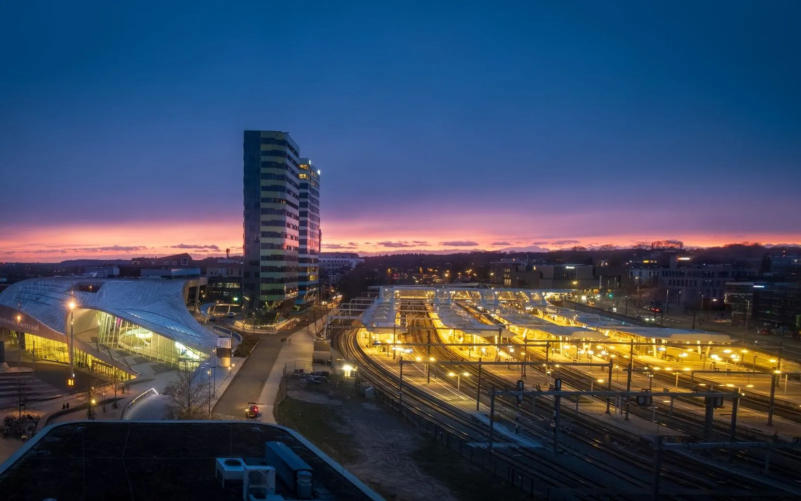 Explore the illuminated Arnhem Central Station at sunset, showcasing urban architecture in the Netherlands.