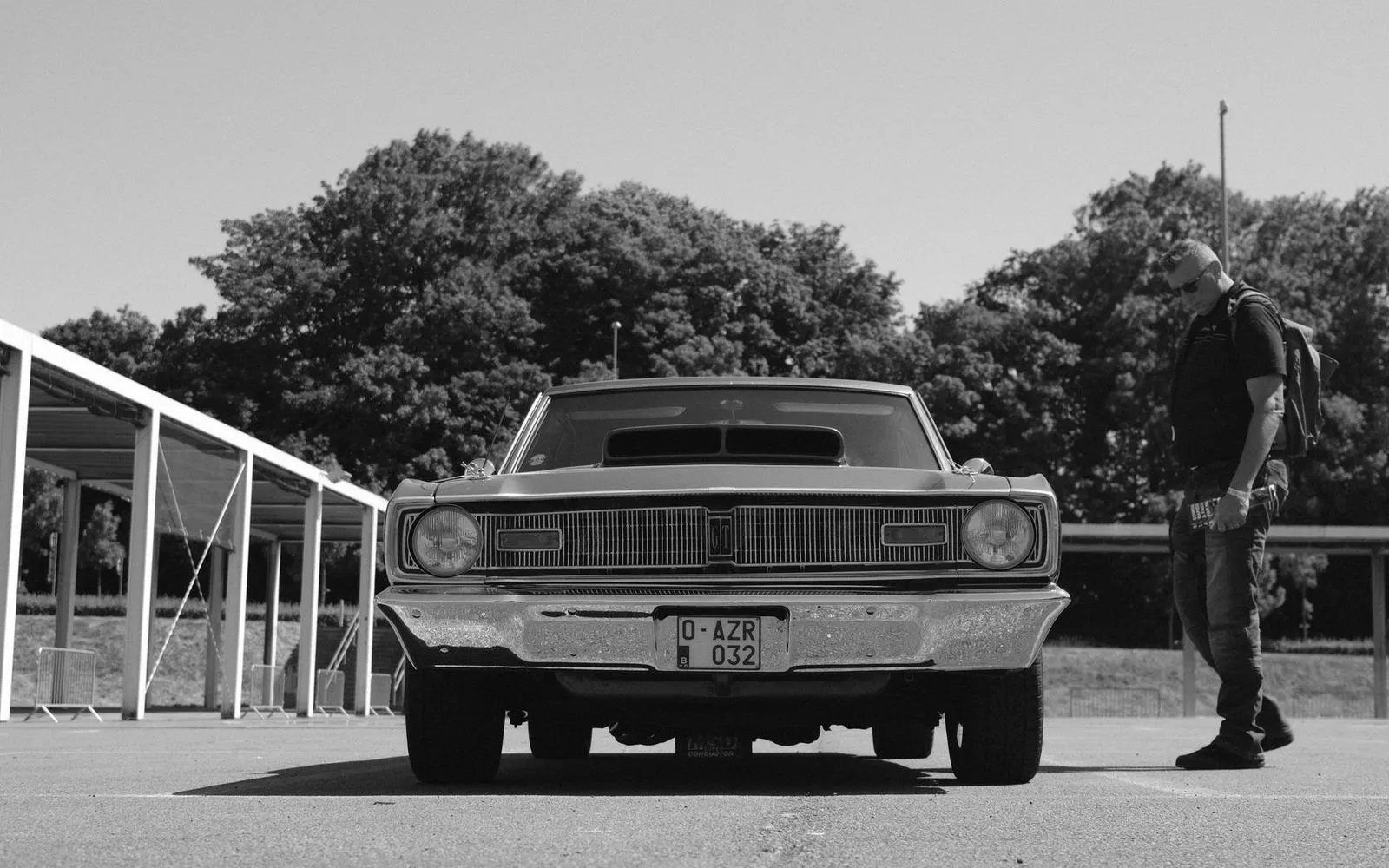 Black and white photo of a vintage Dodge Dart with a man standing nearby in Kortrijk, Belgium.