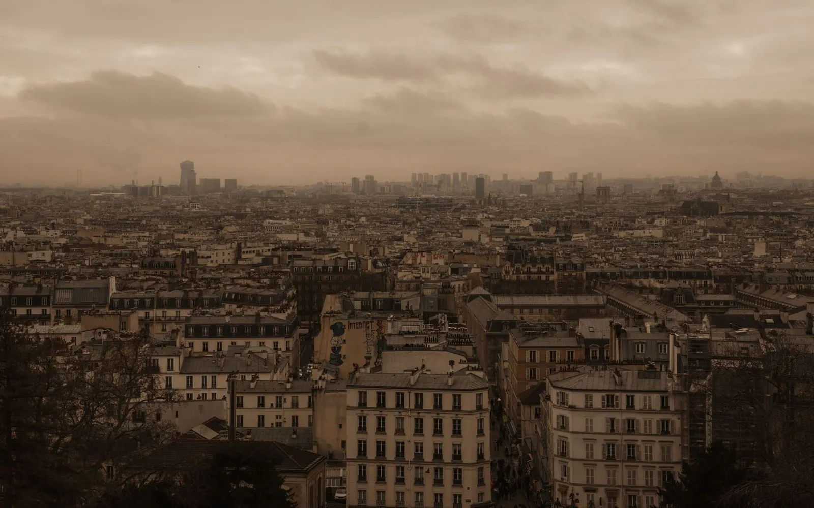 Dramatic view of Paris cityscape with iconic rooftops under moody, overcast skies.